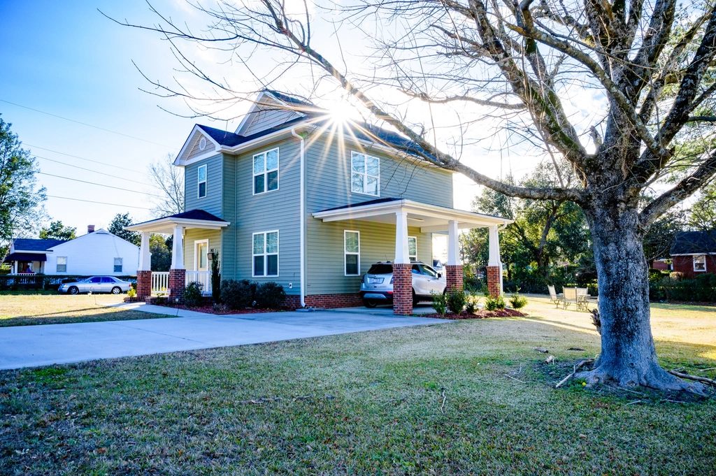 Light blue two story home with a covered porch behind a large shade tree